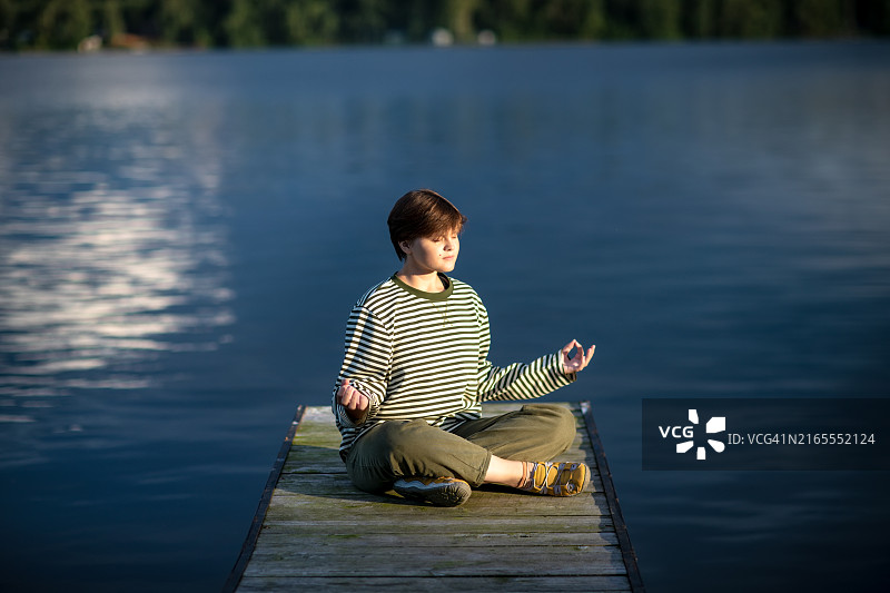 在黄昏时分寻找宁静和正念：湖边木制码头上闭着眼睛的短发少女图片素材