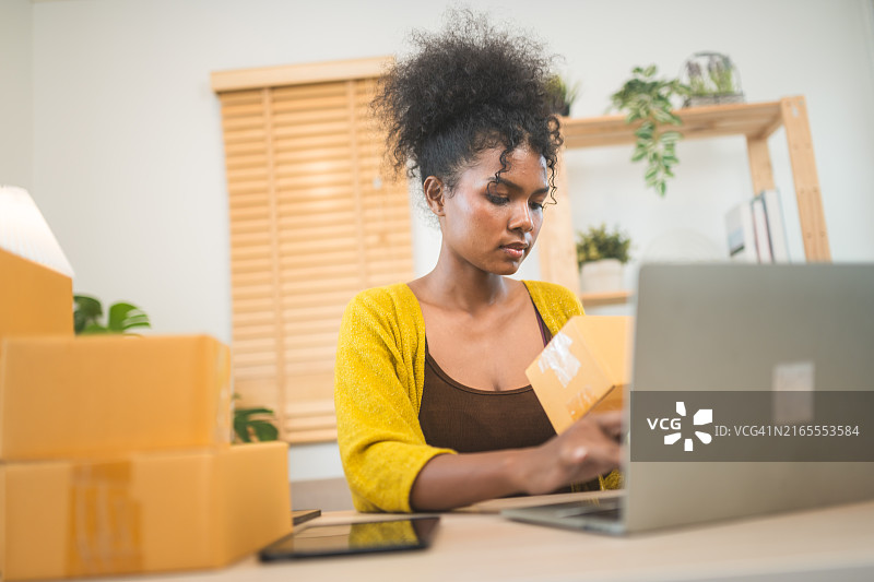 女人在家庭办公室的桌旁工作，处理包裹并使用笔记本电脑图片素材