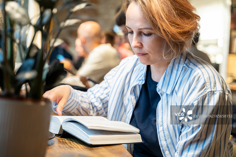 在欧洲舒适的旧咖啡馆里看书的条纹衬衫女人图片素材