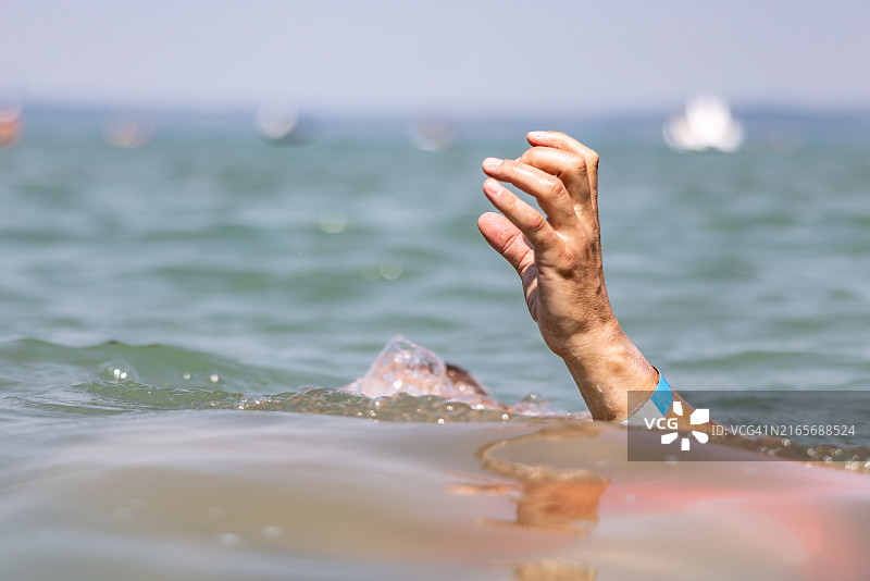 一名年轻游泳者在海滩附近的海中溺水，手臂还在水面上，但他已经开始抽搐，无法呼吸图片素材