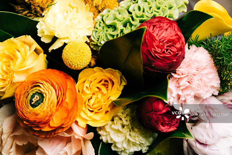 由多种异国情调鲜花组成的明亮花束：红色牡丹玫瑰、绿色鸡冠花、金槌花、康乃馨、黄色玫瑰、橙色波斯毛茛和叶子，美丽的设计背景，俯视拍摄图片素材