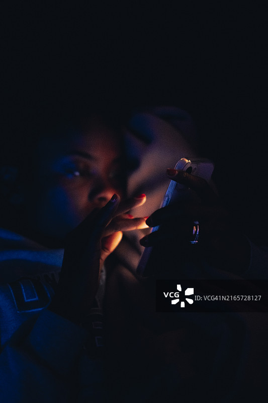 年轻女人在暗室里拿着发光手机的特写，美国得克萨斯州科珀斯克里斯蒂图片素材