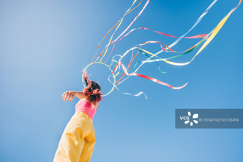 快乐的年轻女子在蓝天下舞动彩色丝带图片素材