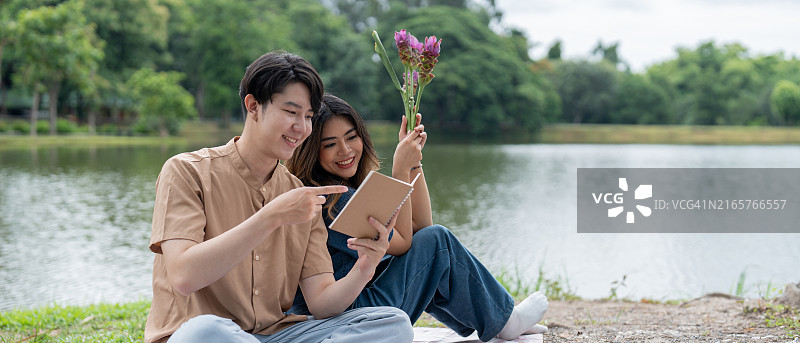 年轻情侣在湖边享受轻松的户外野餐日，鲜花相伴图片素材