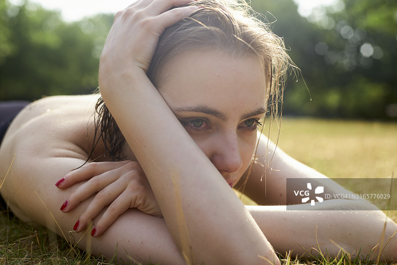 阳光明媚的日子里，一位沉思的女人躺在草地上，头枕双臂图片素材