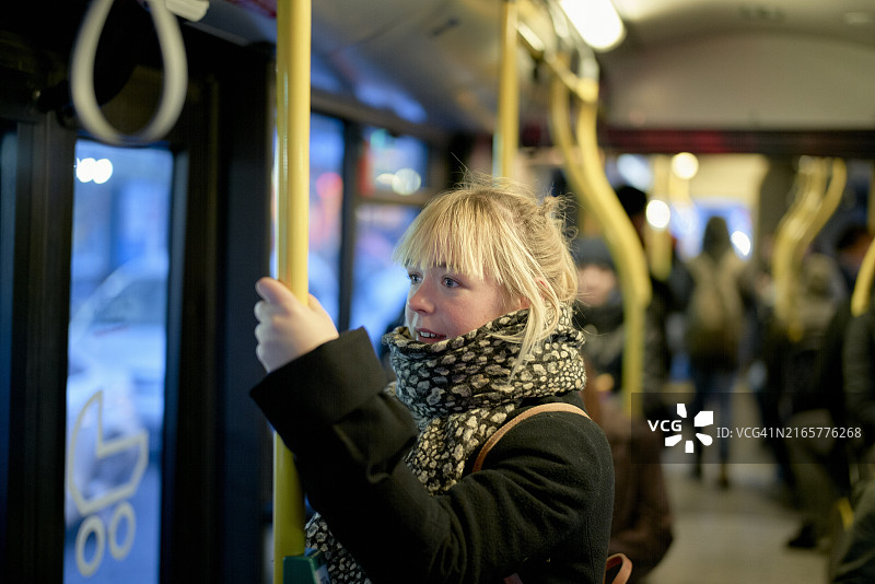 女人在公交车内握着扶手，背景是乘客图片素材