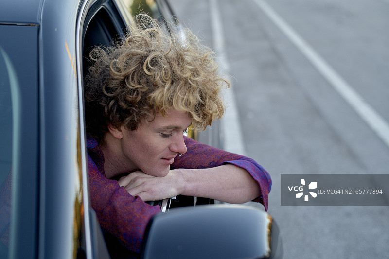 卷发男人 leaning 出车窗，享受着微风图片素材