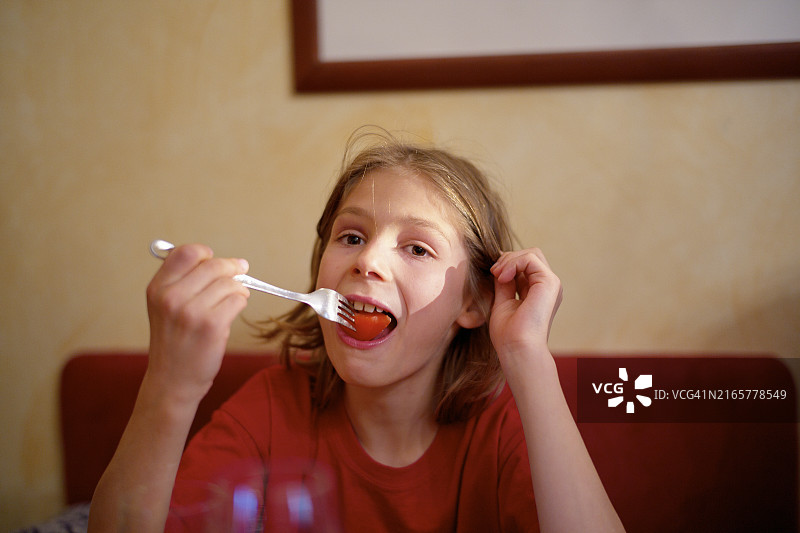 红衣男孩在餐桌旁用叉子吃饭，背景是画作图片素材
