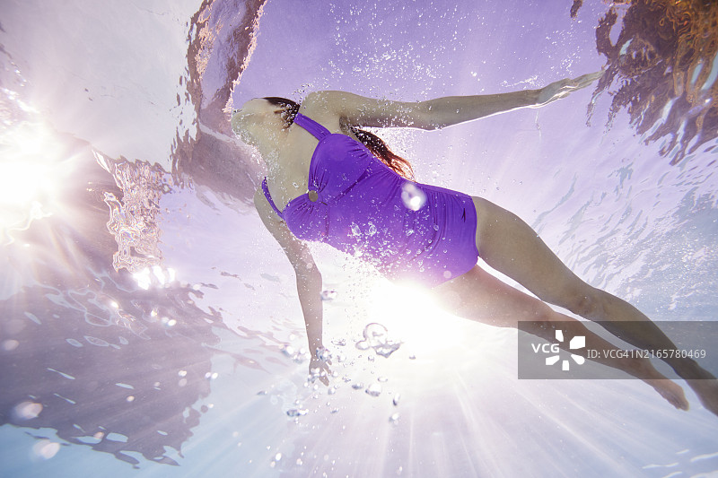 阳光穿过水面，女子在水中游泳的水下景观图片素材