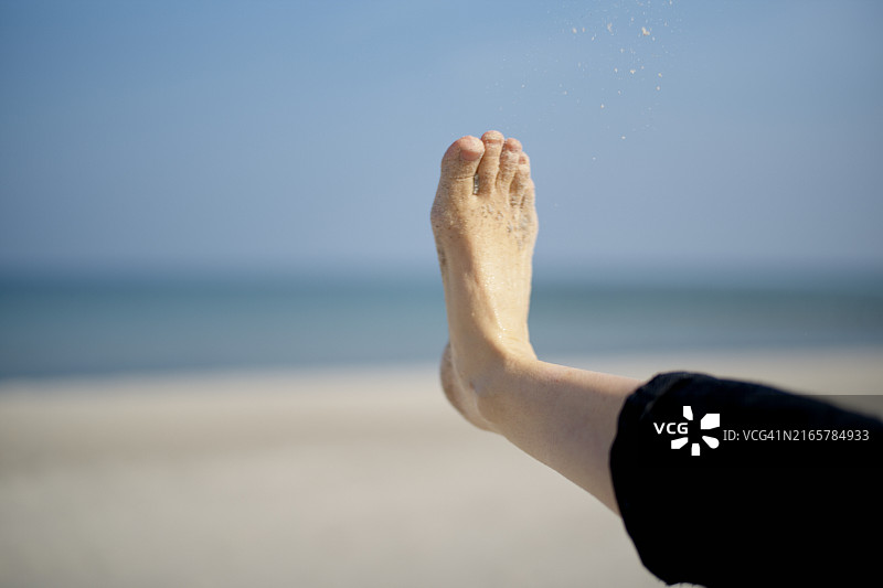 沙滩上的赤脚踢向空中，背景是平静的蓝色大海和晴朗的天空图片素材