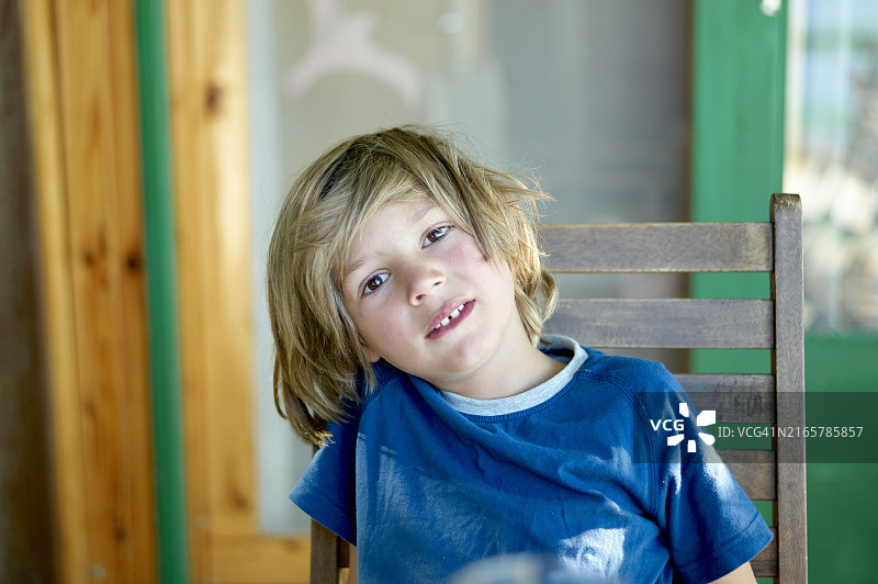 儿童坐在木椅上，面带微笑图片素材