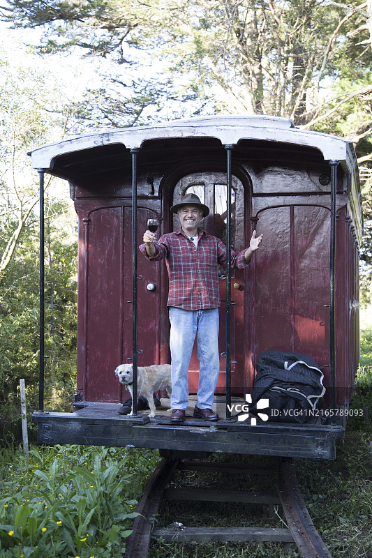 带着狗站在被绿色植物环绕的旧式守车上的男人图片素材