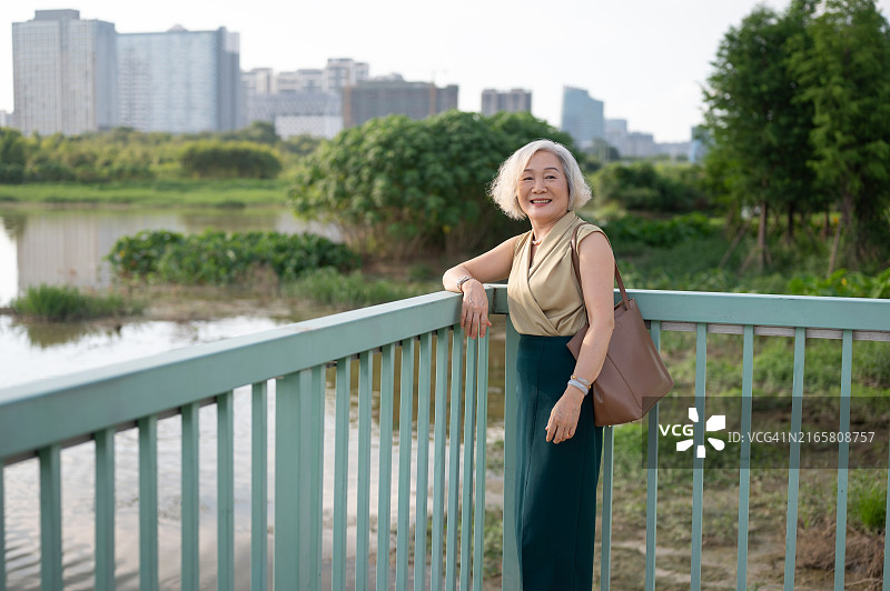 老妇人站在桥上，背景是城市景观图片素材