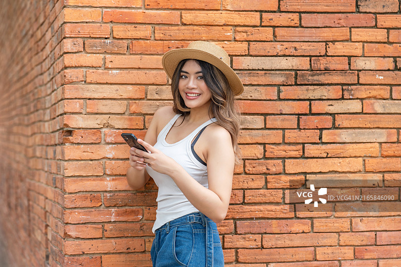 在清迈塔佩门砖墙前拿着手机看向镜头的亚洲女游客图片素材