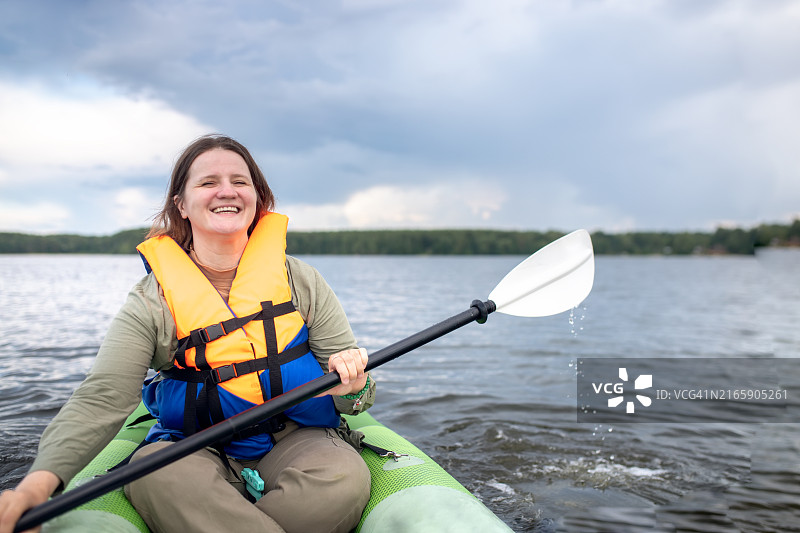 穿救生衣的加大码女人在皮划艇上享受平静的湖面和美丽的景色图片素材