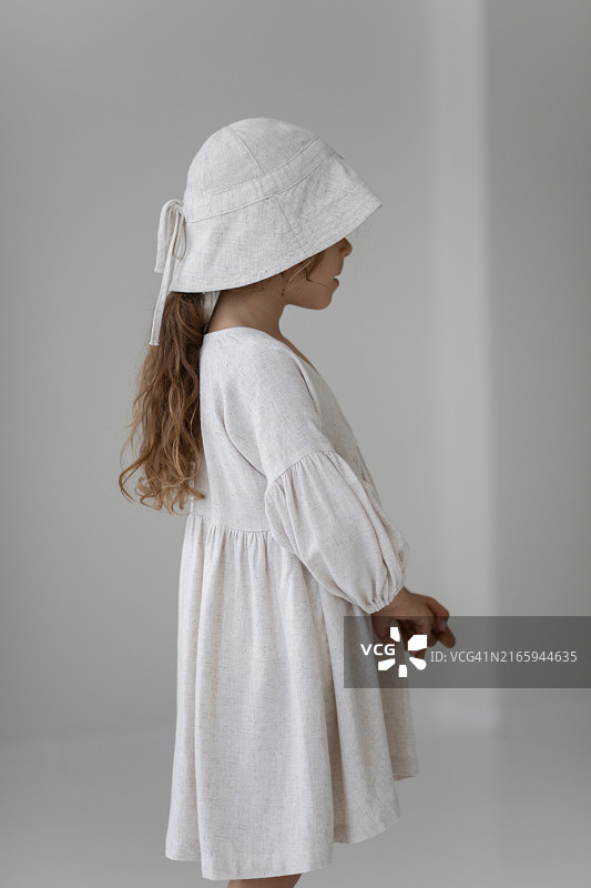 穿着连衣裙和帽子的时尚小女孩在白色背景上摆姿势图片素材