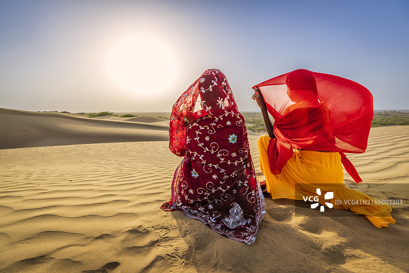 沙漠村庄沙丘上看日落的两位印度女孩图片素材