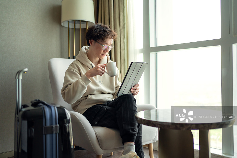 亚洲男子在酒店房间喝咖啡并使用触摸板图片素材