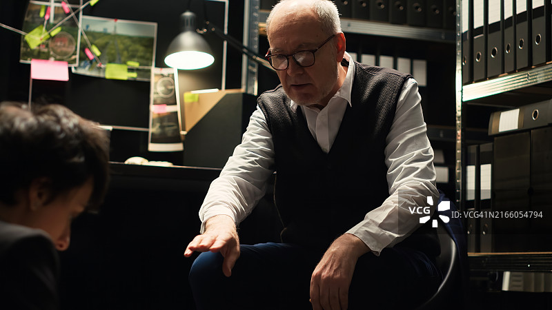 私家侦探在黑暗的办公室里查看监控照片和调查文件图片素材