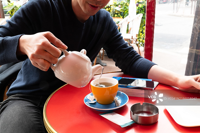 在巴黎咖啡馆露台上倒茶的年轻亚洲男子图片素材