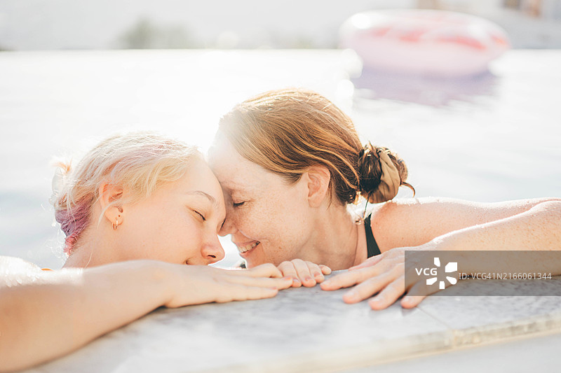 家庭在夏季假期享受酒店游泳池。母女在游泳池中尽情玩乐。图片素材