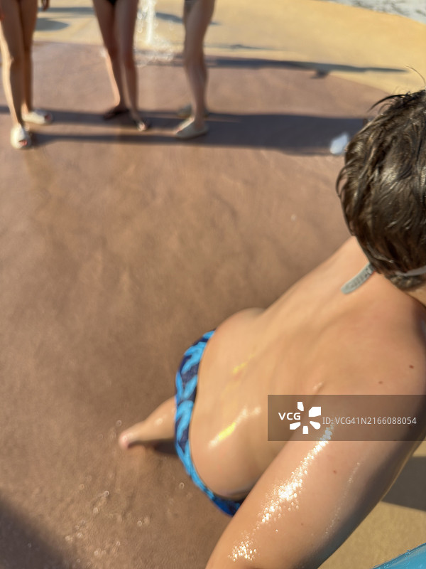 暑假期间在儿童公园的洒水器中玩耍的男孩图片素材