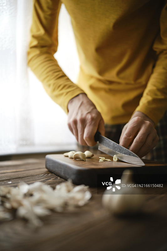 男子在木制砧板上切蒜图片素材