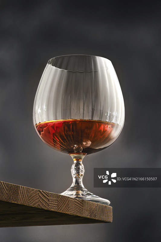 四分之一满的琥珀色干邑的多面玻璃杯，立在乡村木架上图片素材
