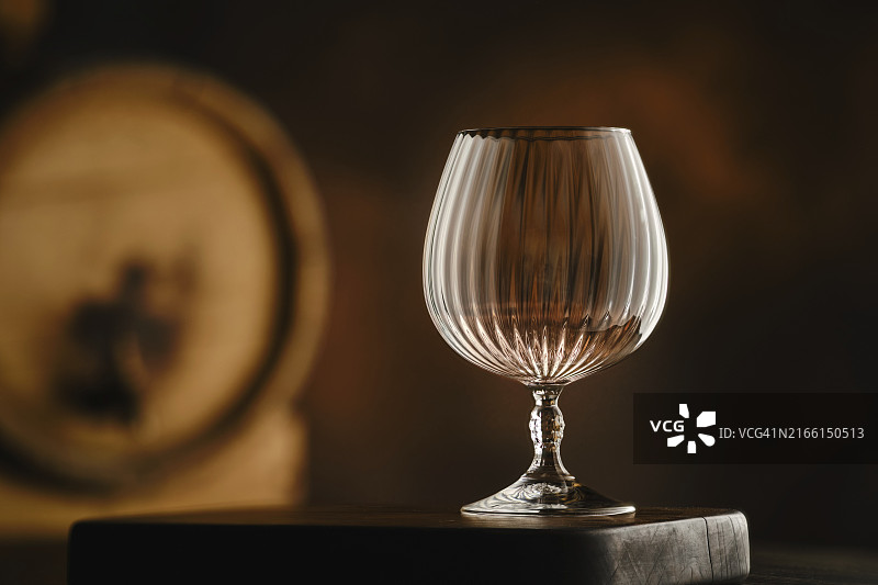在柔和灯光照射下的抛光木质表面上，优雅的水晶白兰地酒杯图片素材