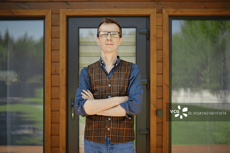 穿衬衫马甲中年男人，现代木屋门前图片素材