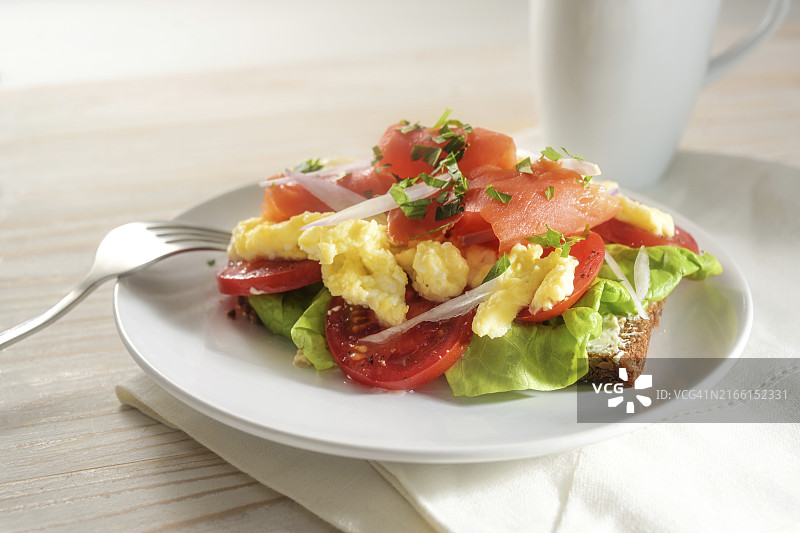 全麦面包搭配番茄、炒鸡蛋和烟熏三文鱼，美味早餐或午餐三明治，焦点选择，窄景深图片素材