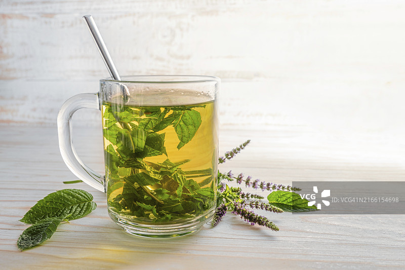 在浅色木桌上的玻璃杯中冲泡新鲜薄荷叶和薄荷花作为凉茶，留白，选择性聚焦，窄景深图片素材