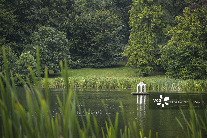 德国波罗的海吕根岛湖上带白色水鸟亭的小型人工岛，岸边有芦苇，还有古老的大树和绿色草坪，欧洲，留白区域图片素材