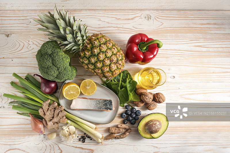 抗炎食物：一系列食材，包括新鲜蔬菜、鱼、水果、坚果和香料，有益于健康的饮食，浅色木质背景，留白，顶部俯视图片素材