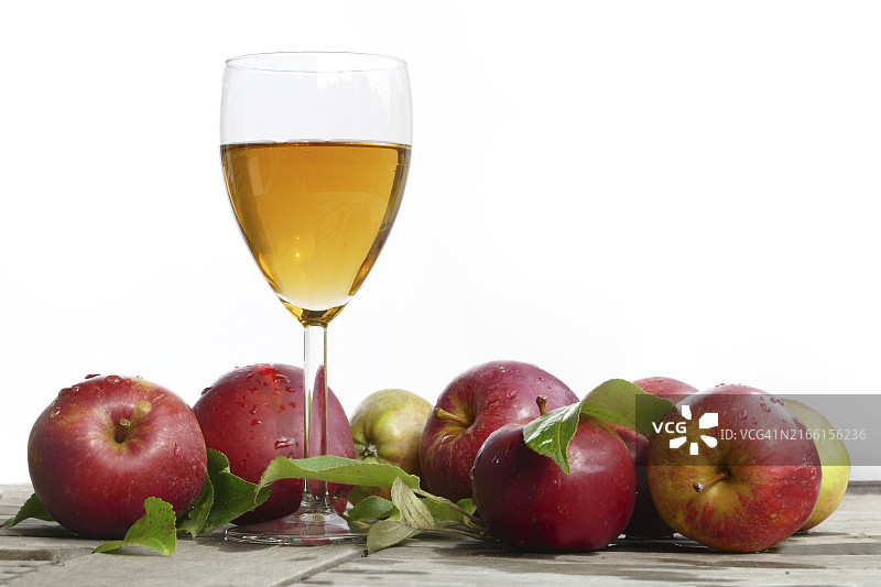 玻璃杯中的鲜榨苹果汁和旧木头上的带叶红苹果，白色背景图片素材