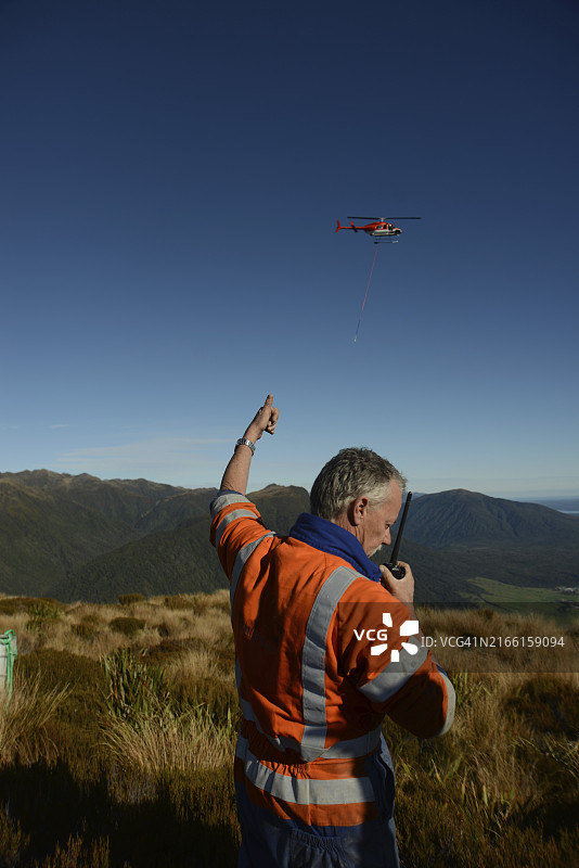 钻井工向直升机挥手，他的团队被带到摩根山顶操作便携式钻机，在新西兰西海岸的Haupiri山谷钻一个10米深的洞，用于地震勘探图片素材