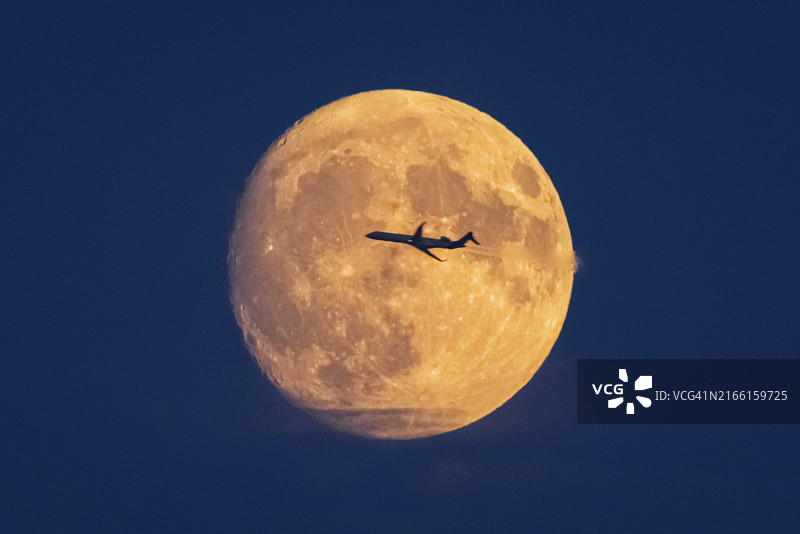 飞机飞过黄橙色满月，德国法兰克福，黑森州，欧洲图片素材