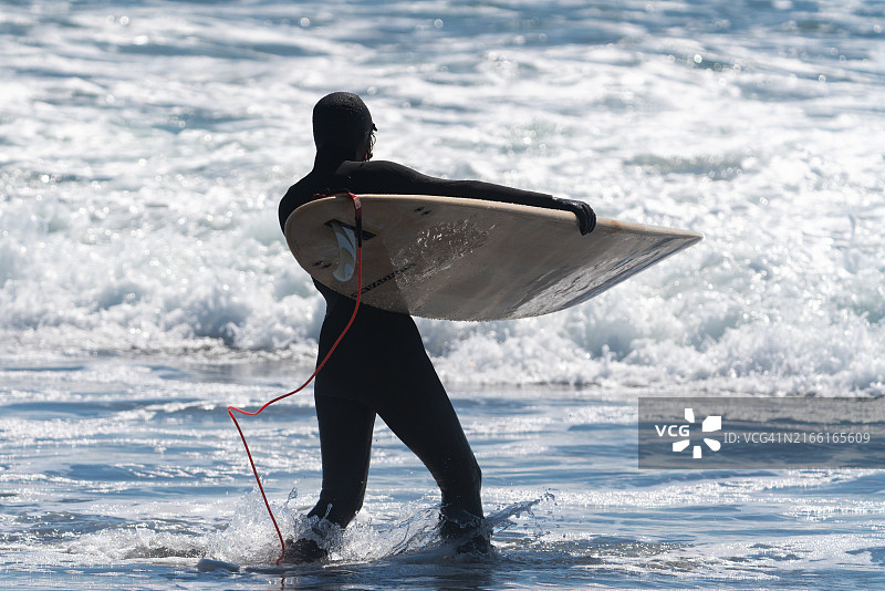 女子身穿潜水服手持冲浪板，勇敢地走向太平洋冰冷的海浪图片素材