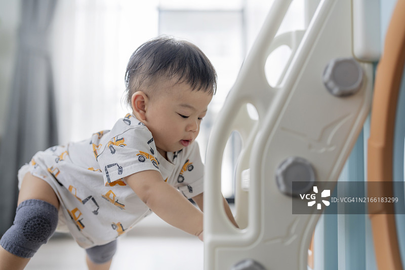 亚洲男婴在家中爬过玩具屋隧道滑梯图片素材