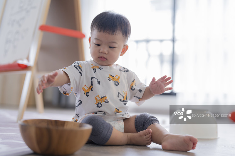 可爱的亚洲男婴在餐具室厨房里专心玩木碗玩具图片素材