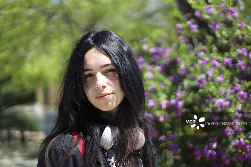 阳光明媚的户外环境中，站在鲜艳花朵附近的黑色长发年轻女子图片素材