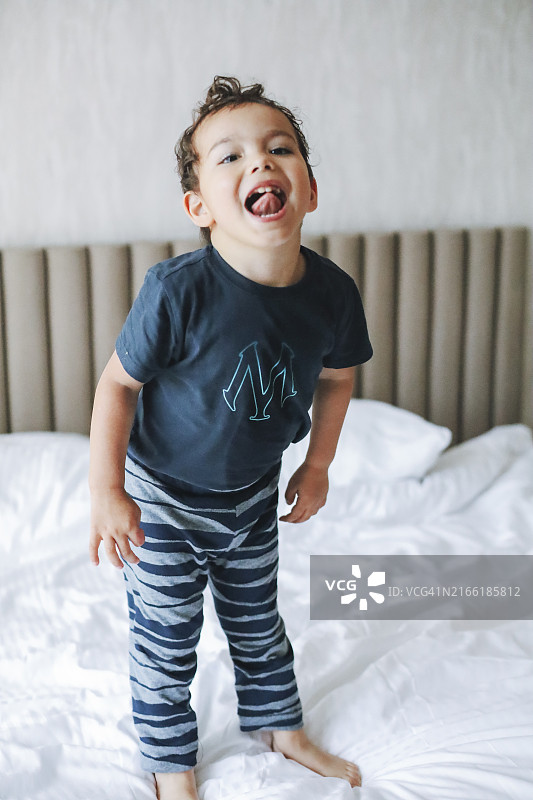 穿着睡衣的男孩在时尚卧室的床上愉快地玩耍图片素材