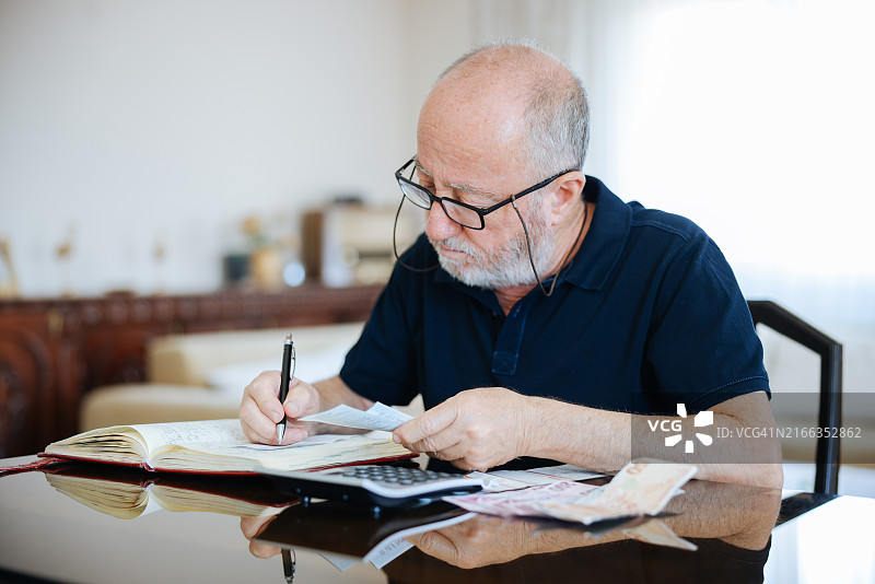 焦虑的老年男人在家管理财务，拿着现金用计算器图片素材