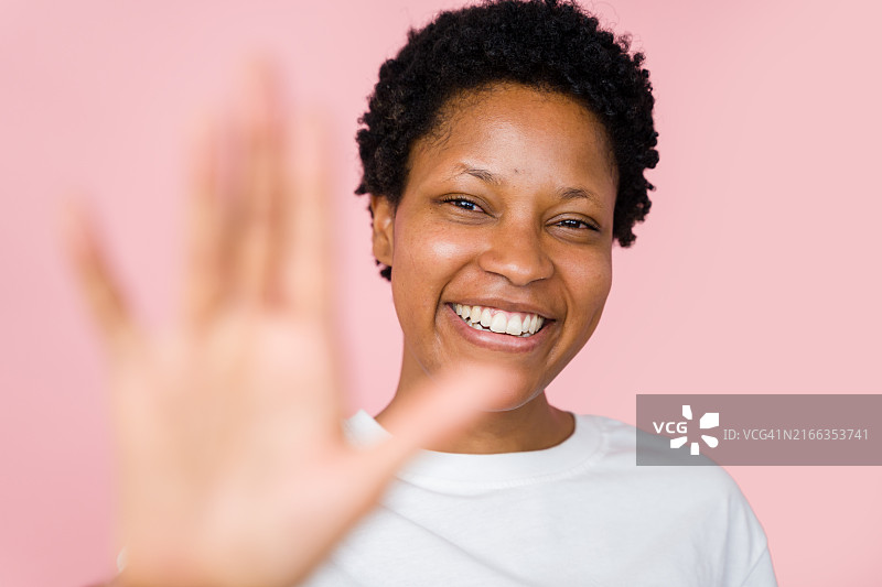 年轻的黑人妇女在粉红色背景下微笑并挥手图片素材