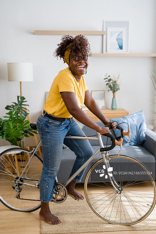 年轻女子在家骑自行车，面带微笑图片素材