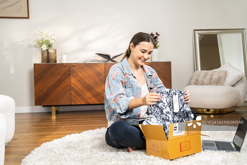 快乐的年轻女子在网上购物后整理衣服图片素材
