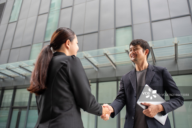 亚洲商人在办公楼前握手商业合作图片素材