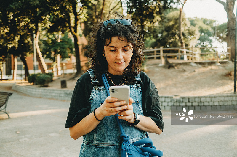 在公园里穿工装裤使用智能手机的女人图片素材