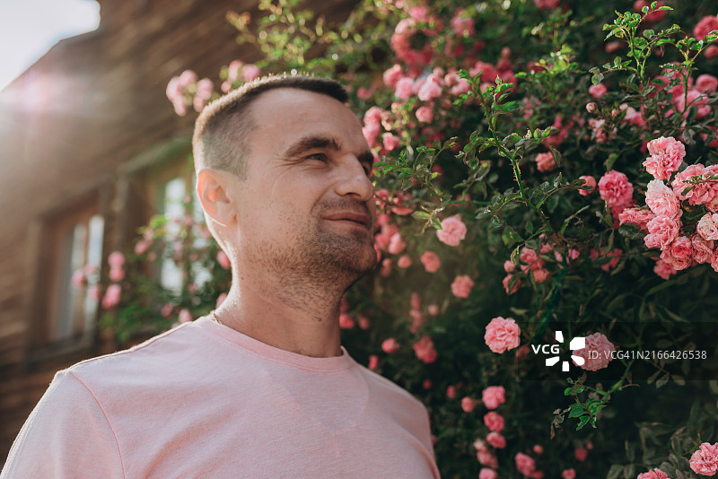 在盛开的粉红玫瑰花束下享受花香的年轻人图片素材