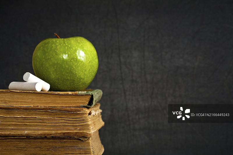 课堂黑板上旧教科书旁的粉笔和青苹果，学校概念图片素材